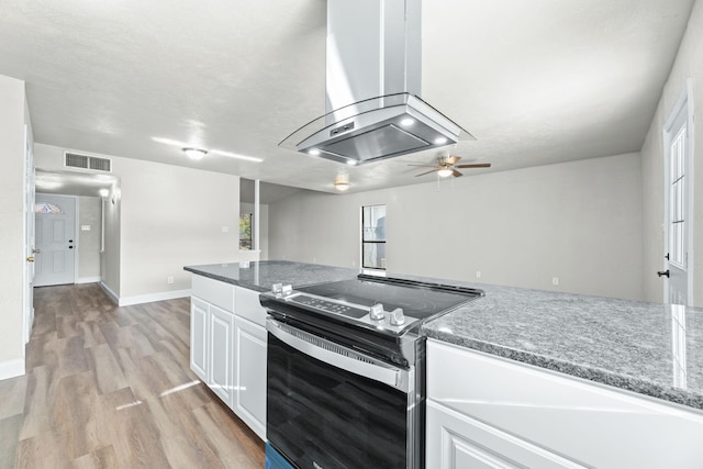 kitchen featuring stainless steel range with electric stovetop, white cabinetry, island range hood, light hardwood / wood-style floors, and dark stone counters