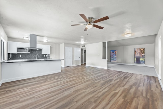 unfurnished living room featuring sink, a textured ceiling, ceiling fan, and light wood-type flooring