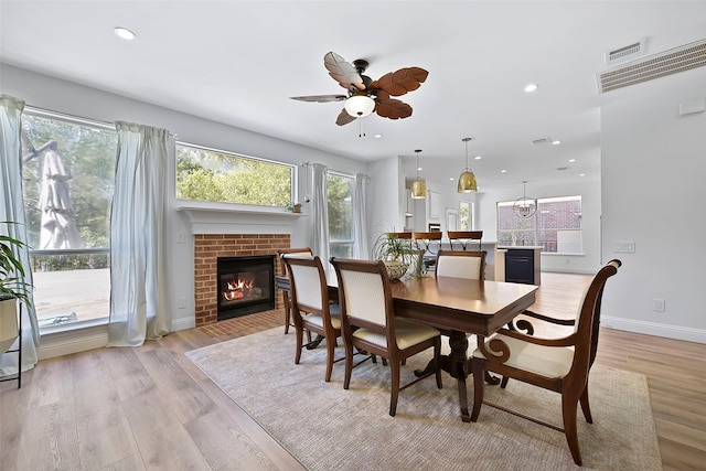 dining space with ceiling fan, a brick fireplace, and light wood-type flooring