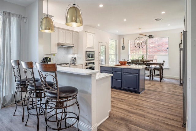 kitchen with hanging light fixtures, stainless steel appliances, wood-type flooring, white cabinets, and a kitchen island