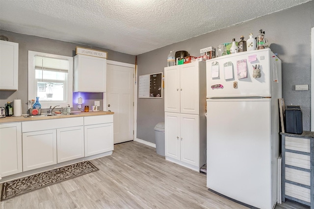 kitchen with white cabinetry, sink, light wood-type flooring, white fridge, and a textured ceiling