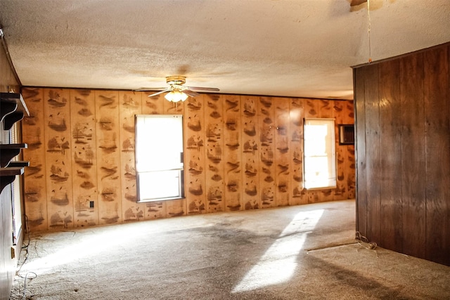 interior space with ceiling fan, carpet, a textured ceiling, and wood walls