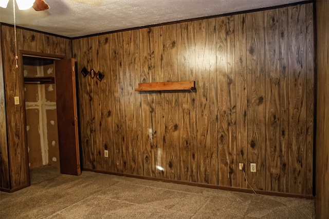 carpeted spare room featuring ceiling fan, wooden walls, ornamental molding, and a textured ceiling