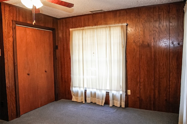 bedroom with wooden walls, carpet floors, ceiling fan, a textured ceiling, and a closet