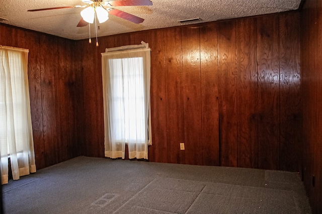 carpeted spare room with ceiling fan, a textured ceiling, and wood walls