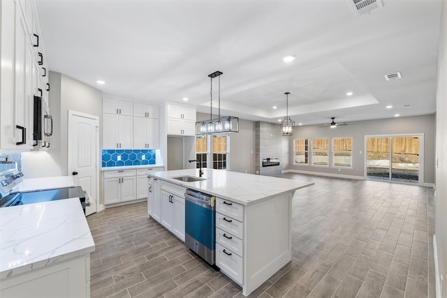 kitchen featuring decorative light fixtures, a center island with sink, appliances with stainless steel finishes, a tray ceiling, and white cabinets