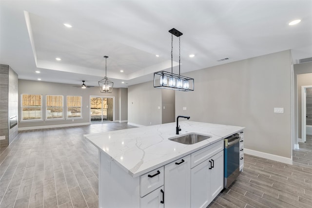 kitchen with white cabinetry, decorative light fixtures, a kitchen island with sink, and sink