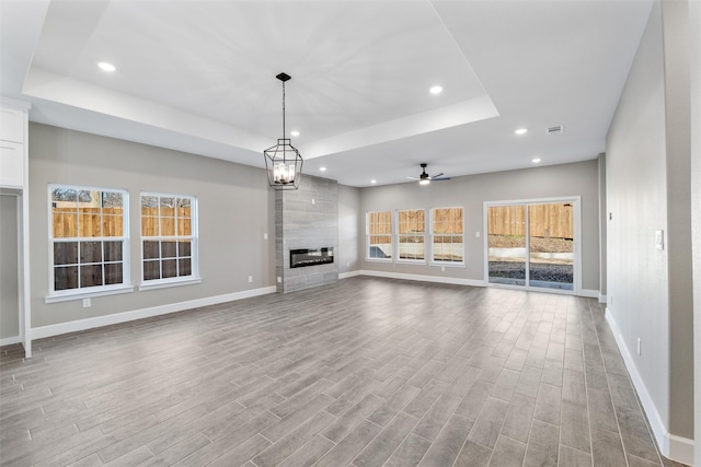 unfurnished living room featuring a tray ceiling, a fireplace, light hardwood / wood-style floors, and ceiling fan with notable chandelier