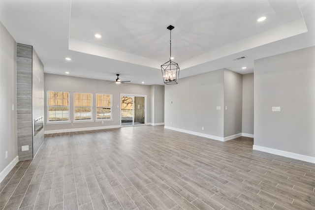 unfurnished living room with a tray ceiling, ceiling fan with notable chandelier, and light wood-type flooring