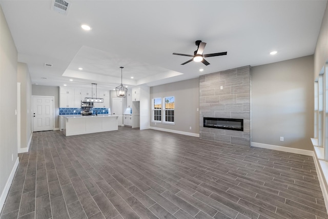 unfurnished living room featuring a raised ceiling, dark hardwood / wood-style flooring, ceiling fan with notable chandelier, and a fireplace