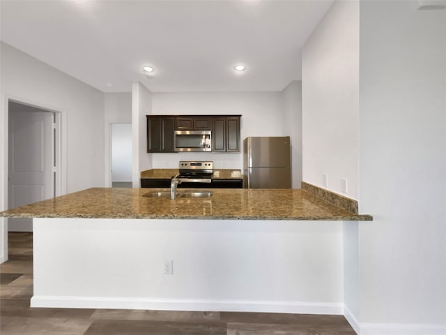 kitchen featuring sink, dark brown cabinets, appliances with stainless steel finishes, kitchen peninsula, and dark stone counters