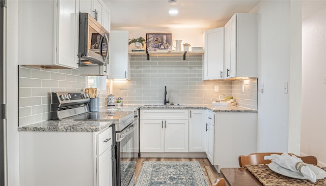 kitchen featuring appliances with stainless steel finishes, sink, white cabinets, light hardwood / wood-style floors, and light stone countertops