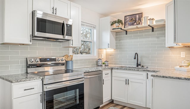 kitchen featuring stainless steel appliances, white cabinetry, sink, and light stone counters