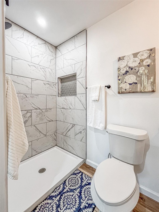 bathroom with a tile shower, hardwood / wood-style floors, and toilet