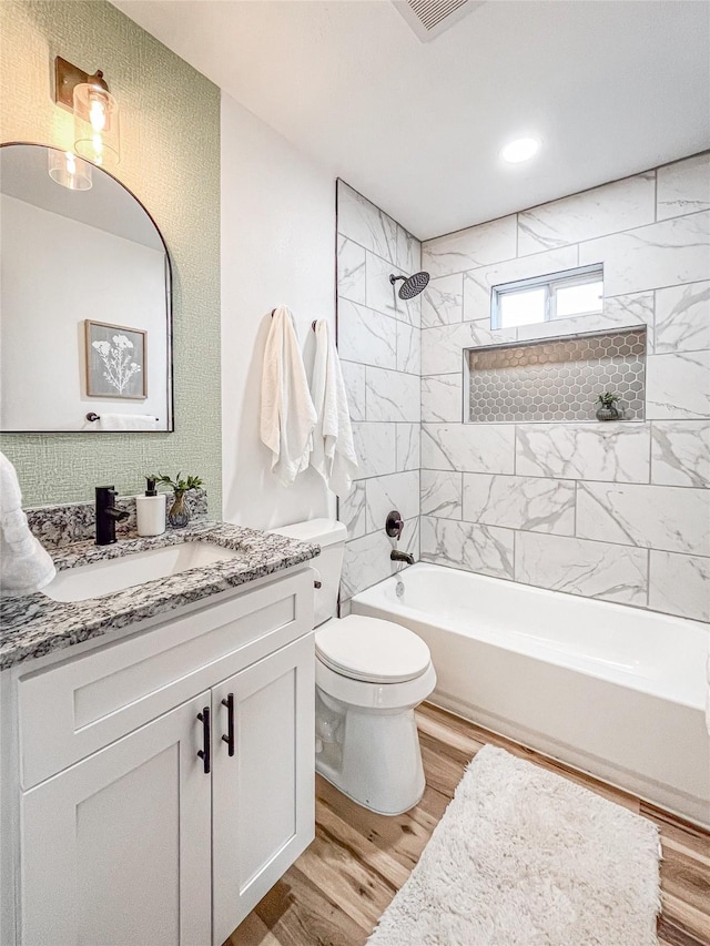 full bathroom featuring wood-type flooring, toilet, tiled shower / bath combo, and vanity