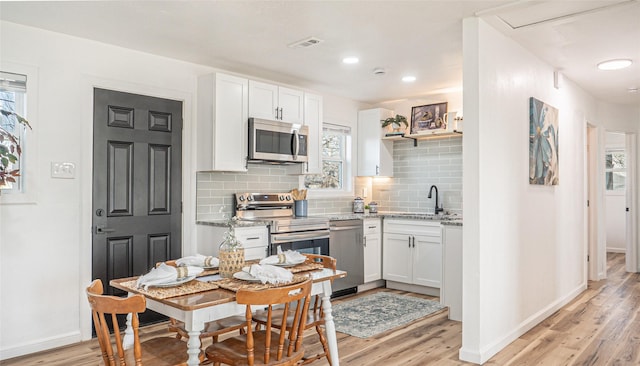 kitchen featuring sink, appliances with stainless steel finishes, light stone countertops, light hardwood / wood-style floors, and white cabinets