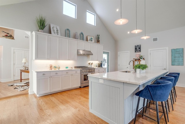 kitchen featuring pendant lighting, sink, white cabinets, high end stainless steel range, and a center island with sink