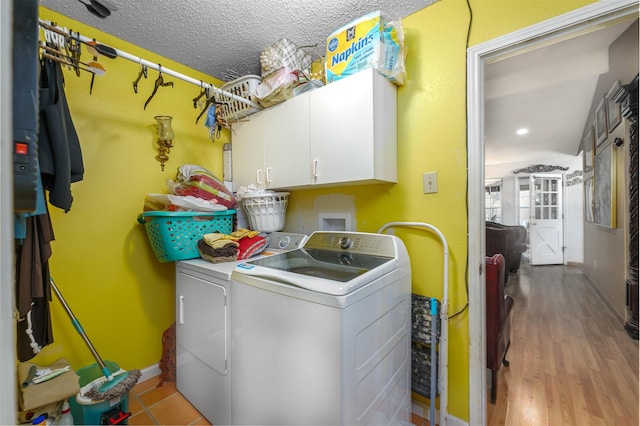 laundry room with cabinets, washing machine and clothes dryer, light hardwood / wood-style floors, and a textured ceiling