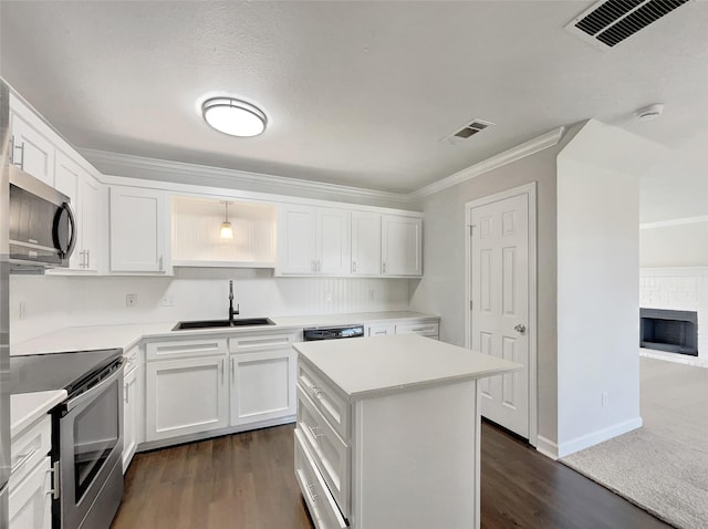 kitchen with a kitchen island, white cabinetry, sink, stainless steel appliances, and a brick fireplace