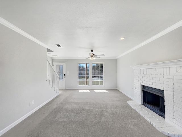 unfurnished living room with crown molding, ceiling fan, a textured ceiling, a brick fireplace, and light colored carpet