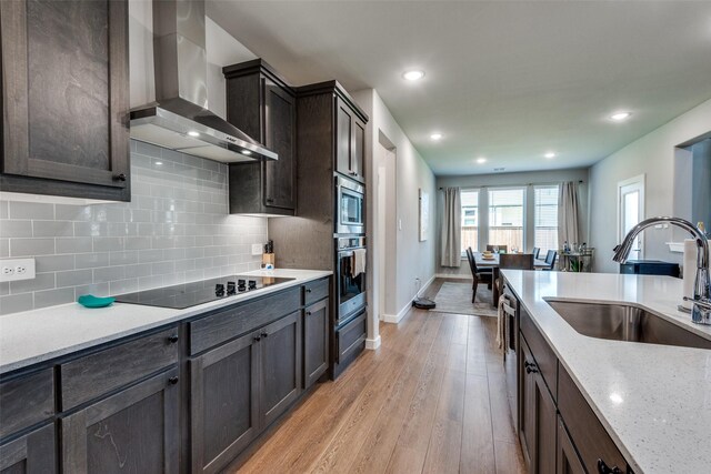 kitchen featuring sink, decorative backsplash, black electric stovetop, wall chimney exhaust hood, and light hardwood / wood-style flooring