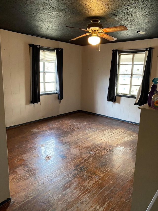 empty room featuring ceiling fan, dark wood-type flooring, and a textured ceiling