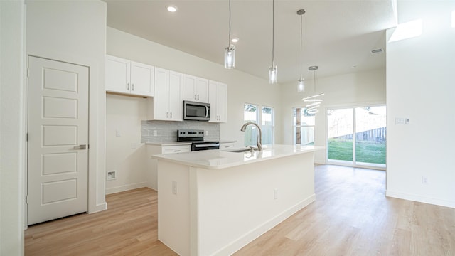 kitchen with appliances with stainless steel finishes, tasteful backsplash, sink, hanging light fixtures, and a kitchen island with sink