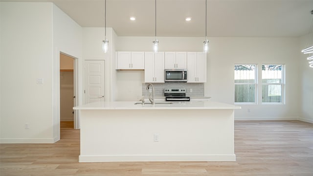 kitchen with appliances with stainless steel finishes, pendant lighting, tasteful backsplash, sink, and a kitchen island with sink