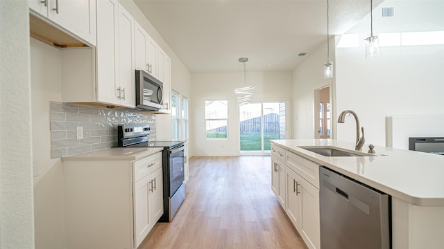 kitchen featuring sink, hanging light fixtures, white cabinets, stainless steel appliances, and backsplash