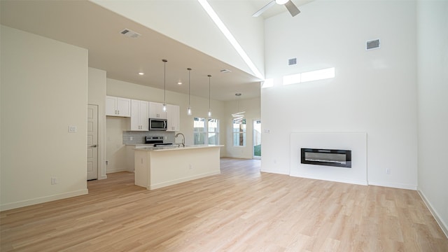 kitchen featuring hanging light fixtures, light wood-type flooring, appliances with stainless steel finishes, an island with sink, and white cabinets