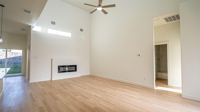 unfurnished living room featuring a high ceiling, ceiling fan, heating unit, and light hardwood / wood-style floors