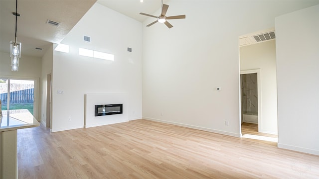 unfurnished living room featuring a towering ceiling, light hardwood / wood-style flooring, and ceiling fan