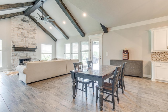 dining room featuring ceiling fan, high vaulted ceiling, a fireplace, beamed ceiling, and light wood-type flooring