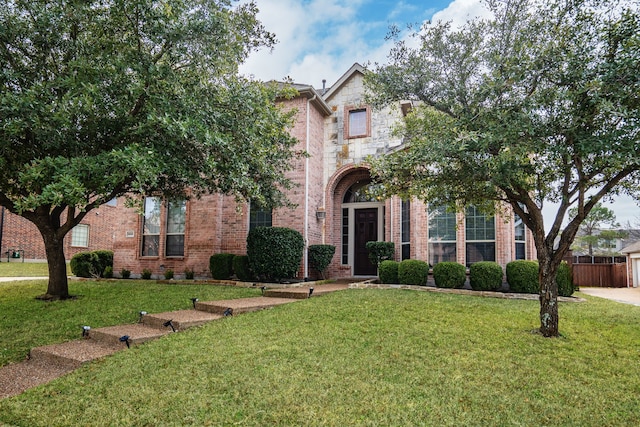 traditional-style house featuring brick siding, fence, stone siding, and a front yard