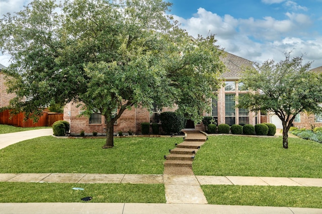 view of property hidden behind natural elements with brick siding, fence, driveway, and a front yard
