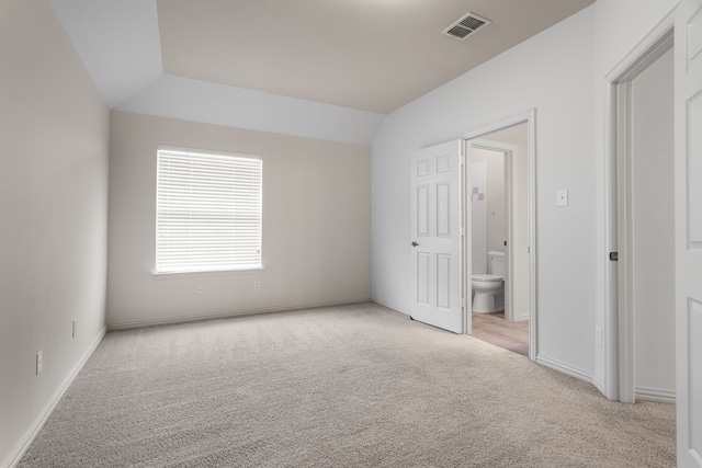 unfurnished bedroom with light carpet, ensuite bath, and lofted ceiling