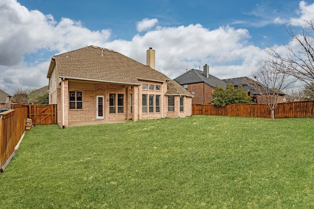 back of property with a yard, brick siding, a fenced backyard, and roof with shingles