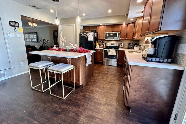 kitchen with pendant lighting, appliances with stainless steel finishes, a center island, a kitchen bar, and decorative backsplash