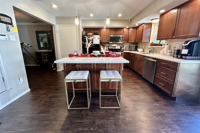 kitchen featuring appliances with stainless steel finishes, hanging light fixtures, a kitchen island, a kitchen bar, and dark hardwood / wood-style flooring