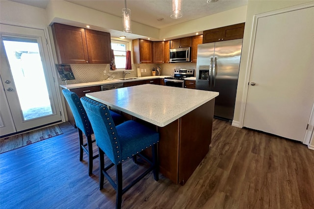 kitchen with sink, a center island, dark hardwood / wood-style flooring, pendant lighting, and stainless steel appliances