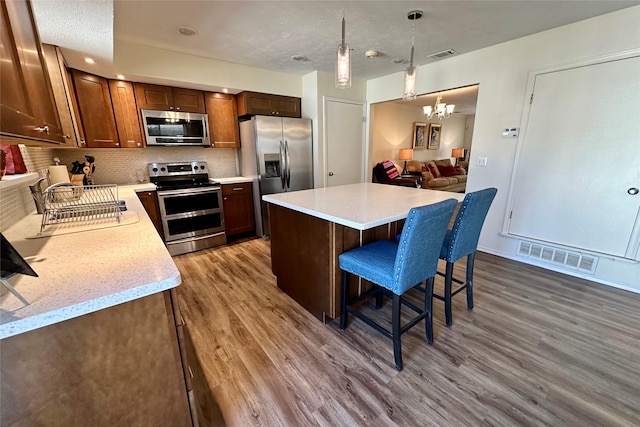 kitchen with pendant lighting, hardwood / wood-style flooring, appliances with stainless steel finishes, backsplash, and a center island