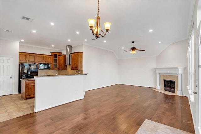 kitchen with decorative light fixtures, wall chimney exhaust hood, light hardwood / wood-style floors, and black appliances