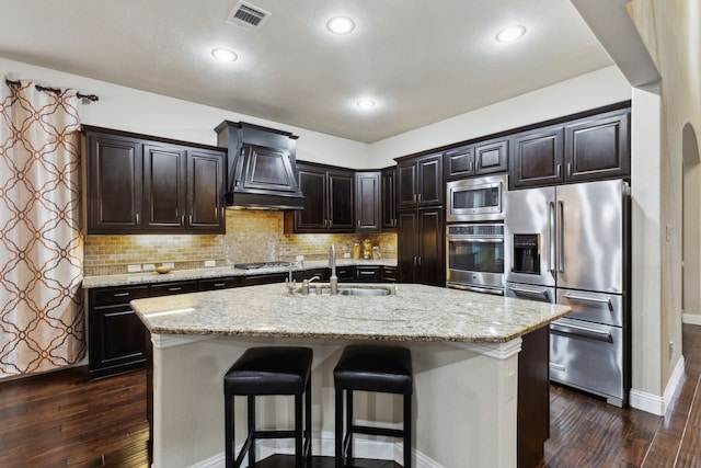 kitchen featuring sink, a kitchen bar, a kitchen island with sink, stainless steel appliances, and custom range hood