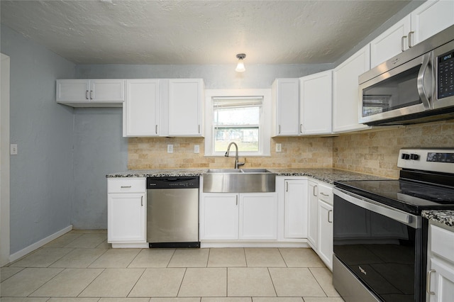 kitchen with sink, stainless steel appliances, dark stone counters, and white cabinets