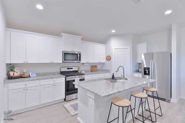 kitchen with an island with sink, stainless steel appliances, sink, and white cabinets