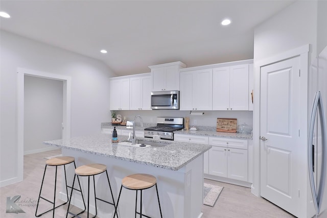 kitchen featuring appliances with stainless steel finishes, white cabinetry, sink, a kitchen island with sink, and light stone countertops