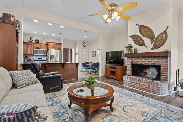 living room with dark hardwood / wood-style flooring, a fireplace, ornamental molding, and ceiling fan