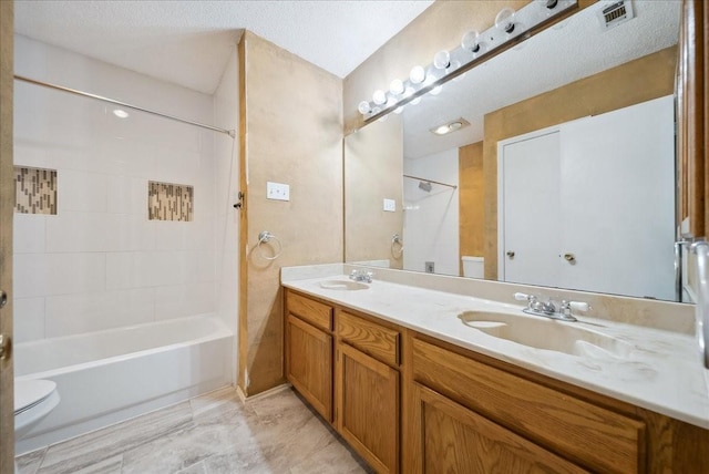 full bathroom with vanity, tiled shower / bath, a textured ceiling, and toilet