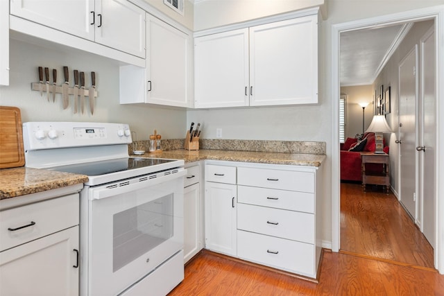 kitchen with white cabinets, ornamental molding, electric range, light stone countertops, and light wood-type flooring