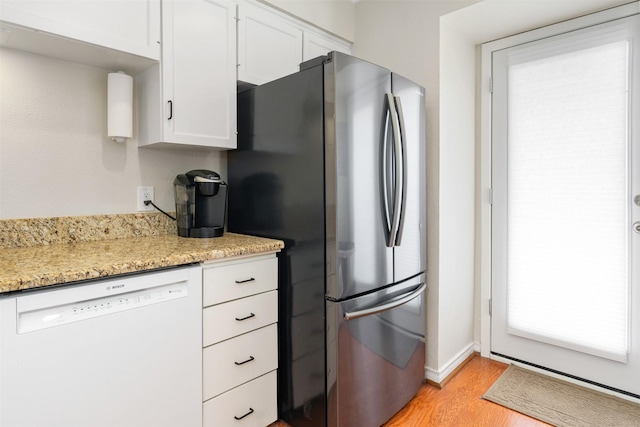 kitchen with light stone counters, light hardwood / wood-style flooring, stainless steel refrigerator, white dishwasher, and white cabinets